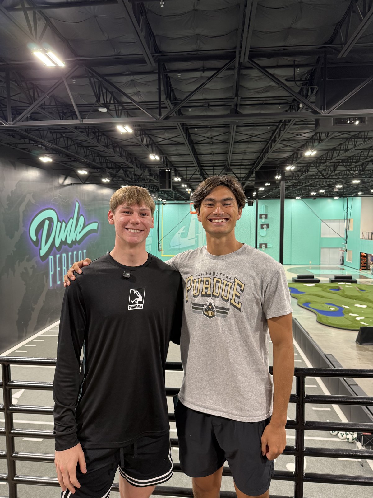 Cam Hazzard and a friend inside Dude Perfect headquarters in front of the logo